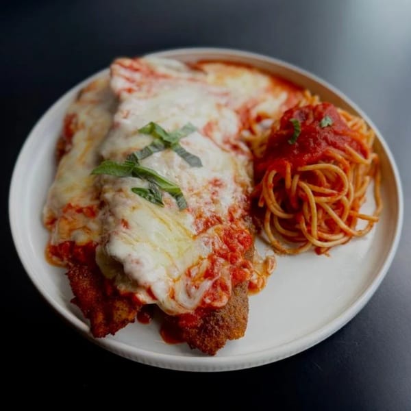 Chicken parmesan with melted mozzarella, marinara sauce, fresh basil, and a side of spaghetti.