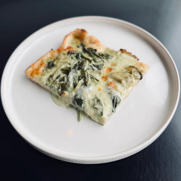 A slice of creamy green pizza with spinach and cheese on a white plate.