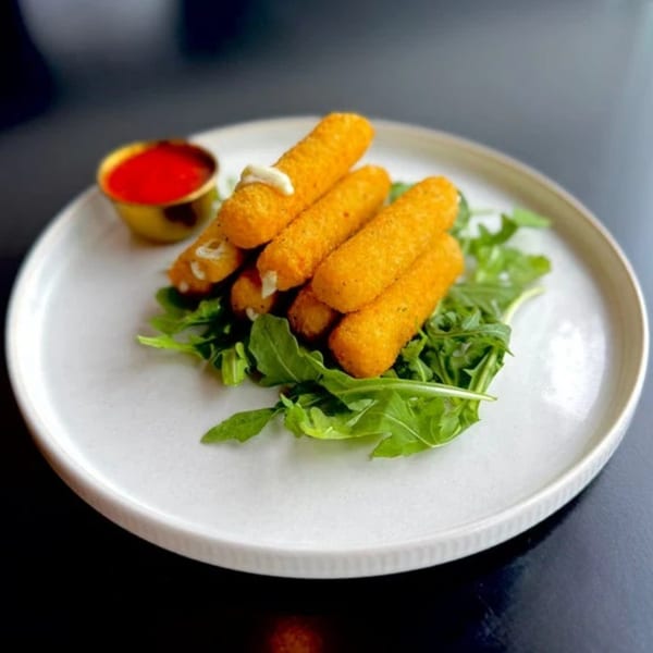 Golden-brown mozzarella sticks with a side of red dipping sauce on a bed of fresh arugula.