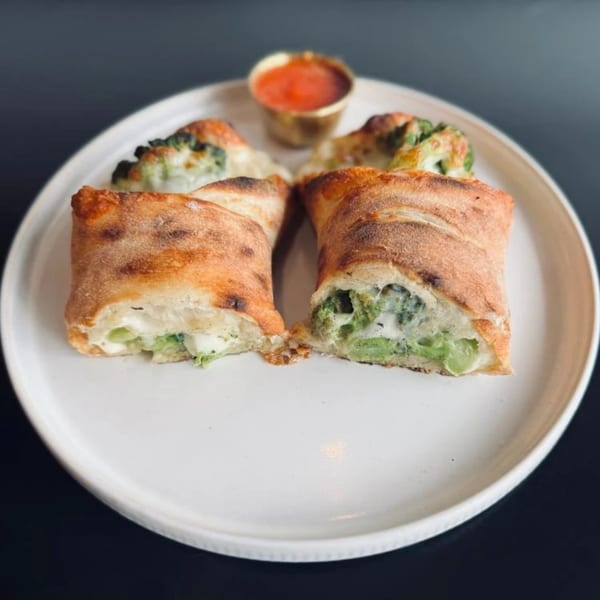Two golden-brown strombolis, cut open to reveal melted cheese and broccoli, with a side of marinara sauce.