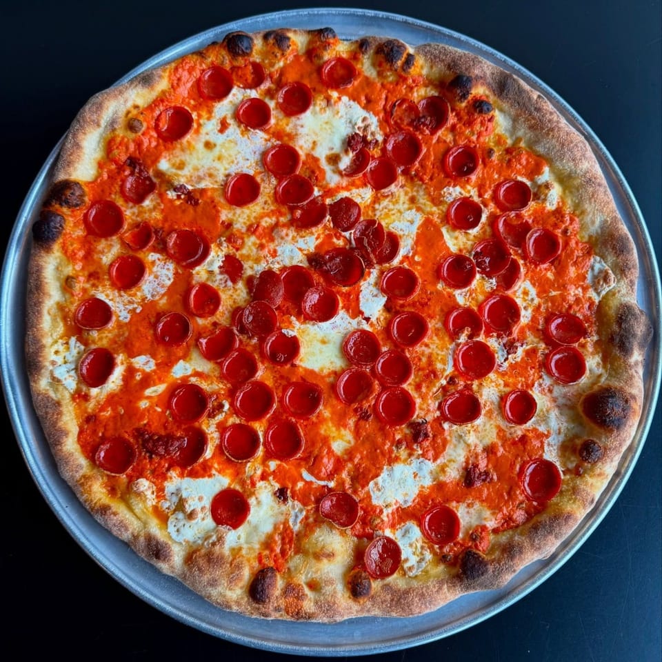 A whole pepperoni pizza with white cheese and red sauce on a metal tray.