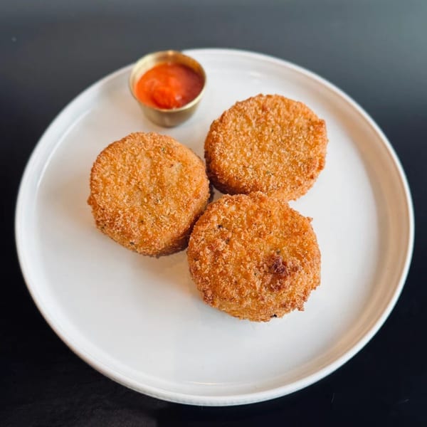 Three golden-brown fried patties with a side of red dipping sauce on a white plate.