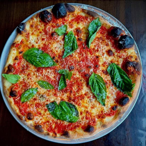 A whole margherita pizza with fresh basil leaves and grated cheese on a metal tray.