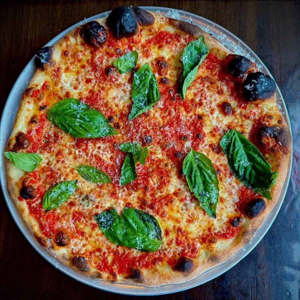 A whole margherita pizza with fresh basil leaves and grated cheese on a metal tray.