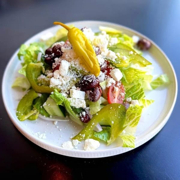 A vibrant Greek salad with lettuce, tomatoes, olives, feta, green peppers, and a yellow pepperoncini.